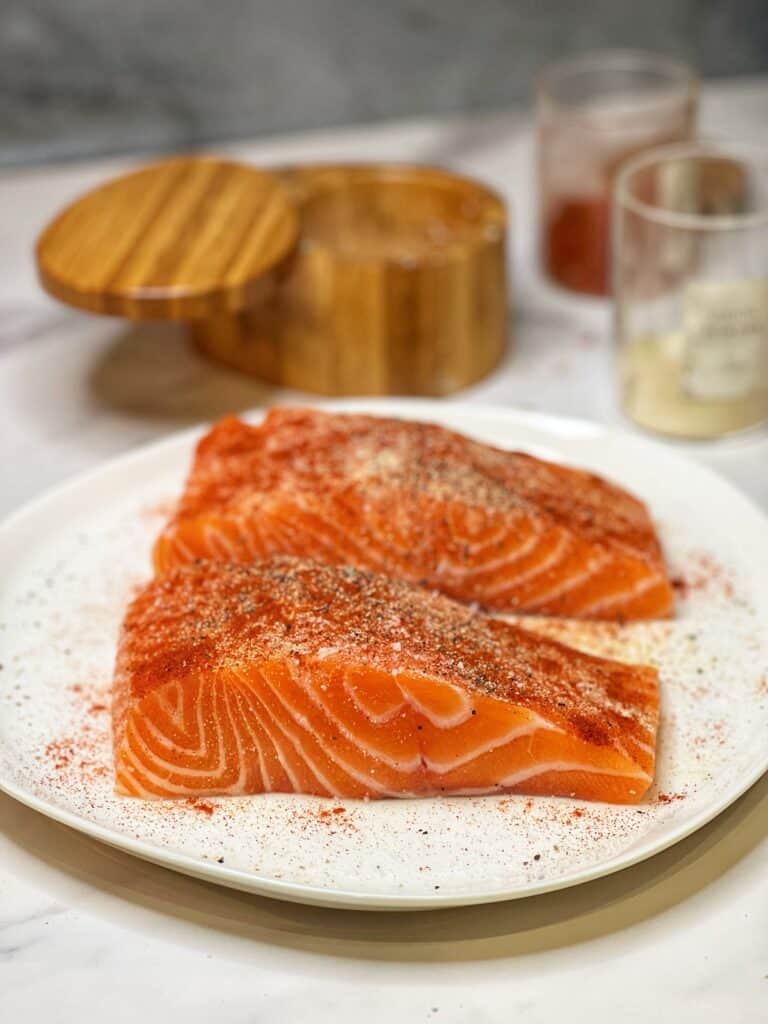 Two seasoned salmon filets sitting on a white plate.