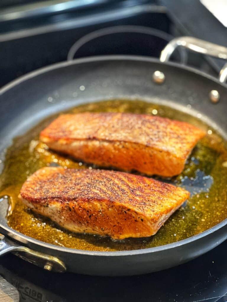 Two salmon filets searing in a non-stick pan.