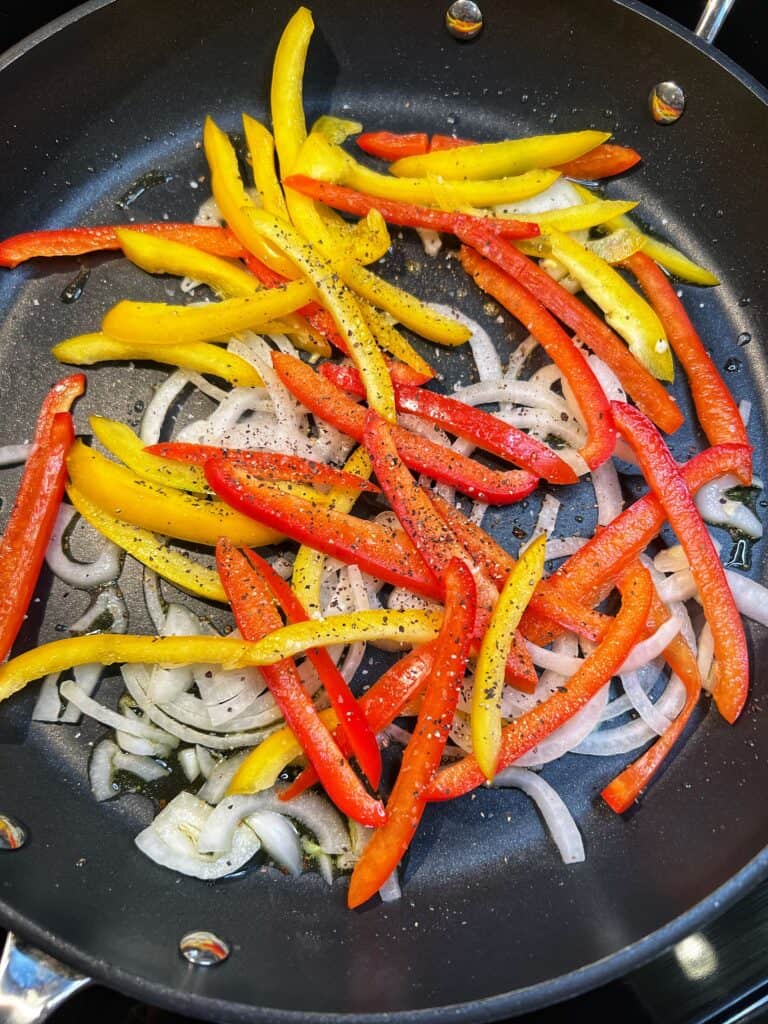 Thinly sliced onions and peppers sautéing in olive oil in a non-stick pan.