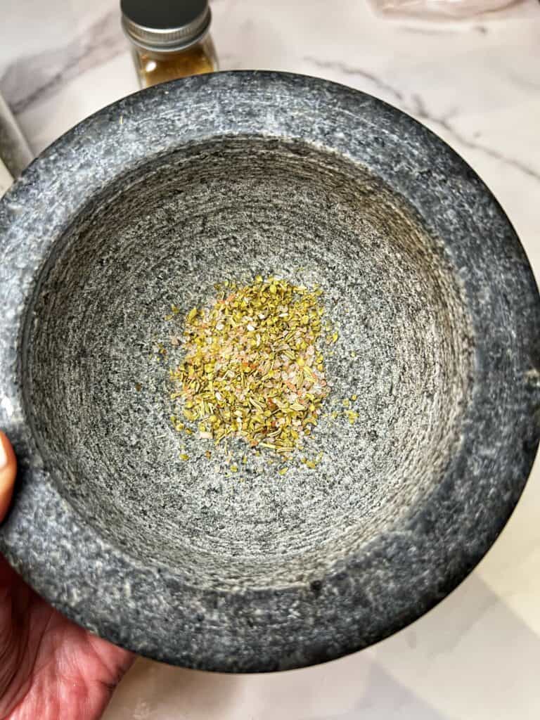 Using a mortar and pestle to grind the fennel and cumin seeds with dried oregano and salt.