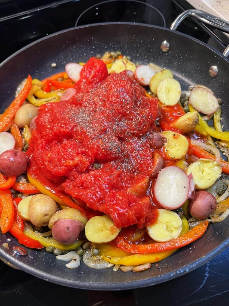 Crushed tomatoes added to a pan of sautéed onions and bell peppers and baby potatoes.