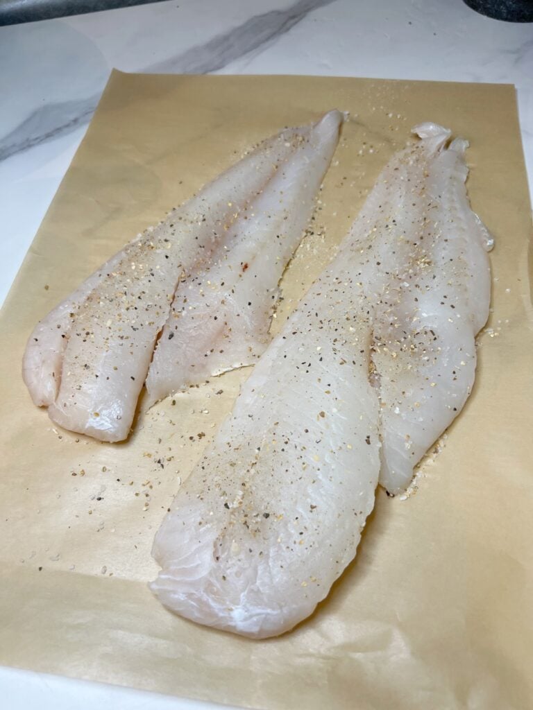 Two cod filets sitting on a piece of brown parchment paper.