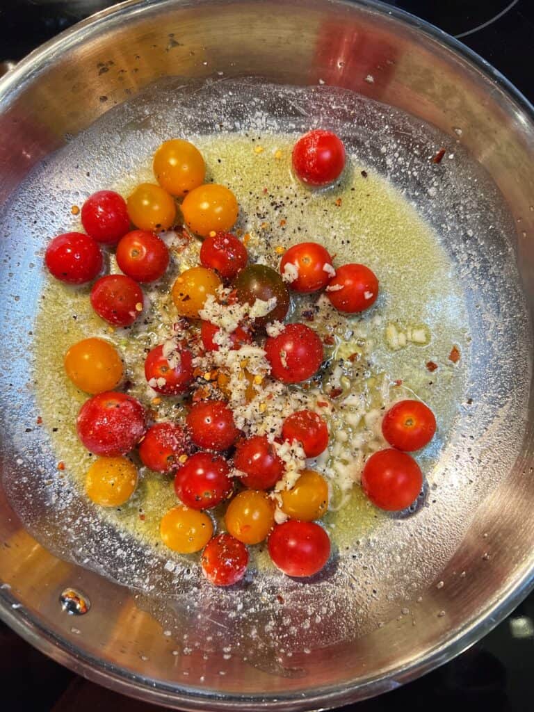 Cherry tomatoes and minced garlic sautéing in olive oil and butter in a stainless steel pan.