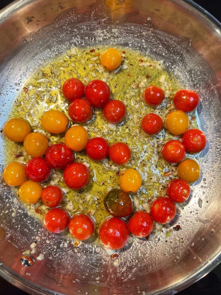 Cherry tomatoes starting to burst in a stainless steel pan of olive oil and butter.