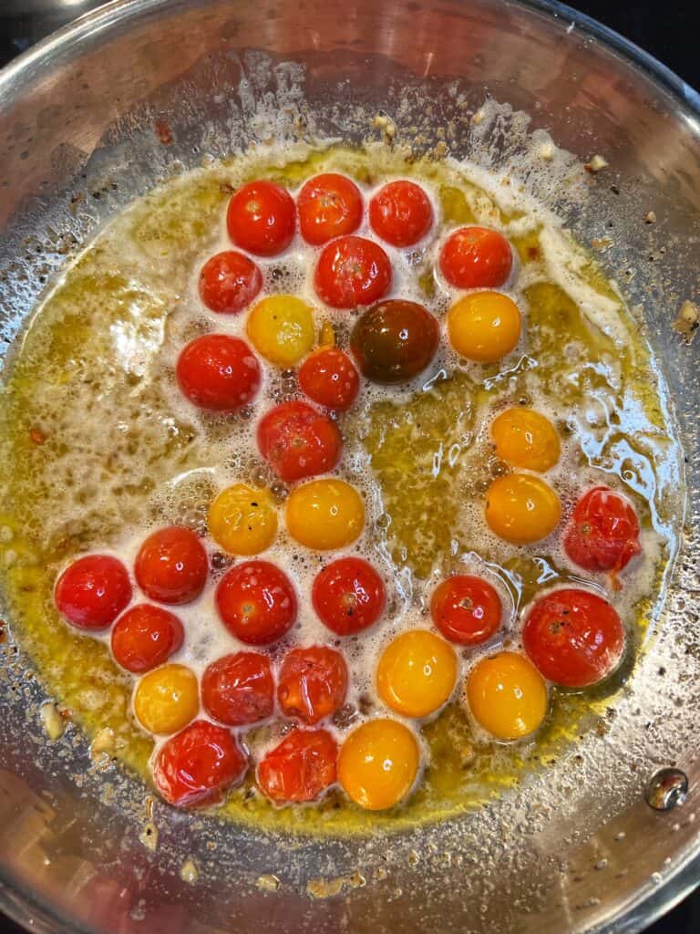 Wine wine added to a stainless steel pan with bursting cherry tomatoes.
