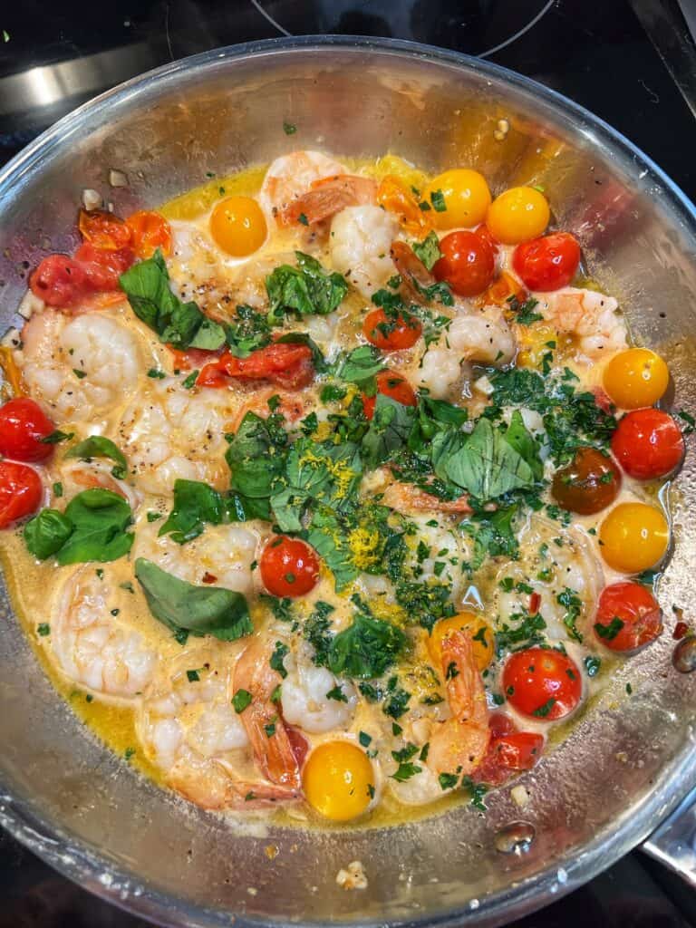 Fresh basil and parsley added to a pan of sautéed cherry tomatoes and cooked shrimp.