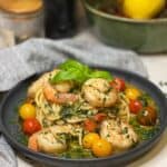 A round, charcoal-colored plate holding shrimp scampi spaghetti that is garnishedwith fresh herbs.