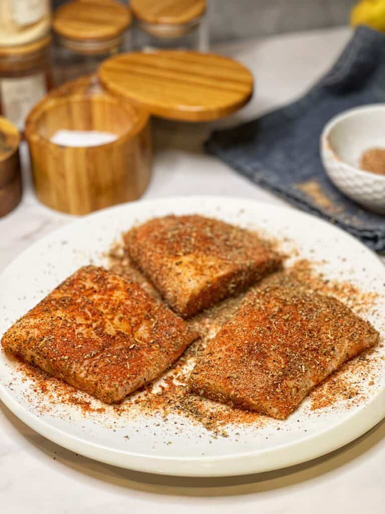 Three cod filets seasoning with blackening seasoning, sitting on a white plate