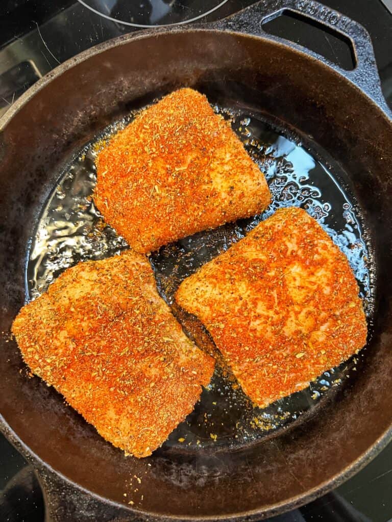 Three seasoned cod filets searing in a cast iron pan.