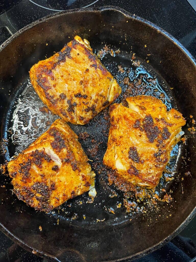 Three blackened cod filets seared in a cast iron pan.