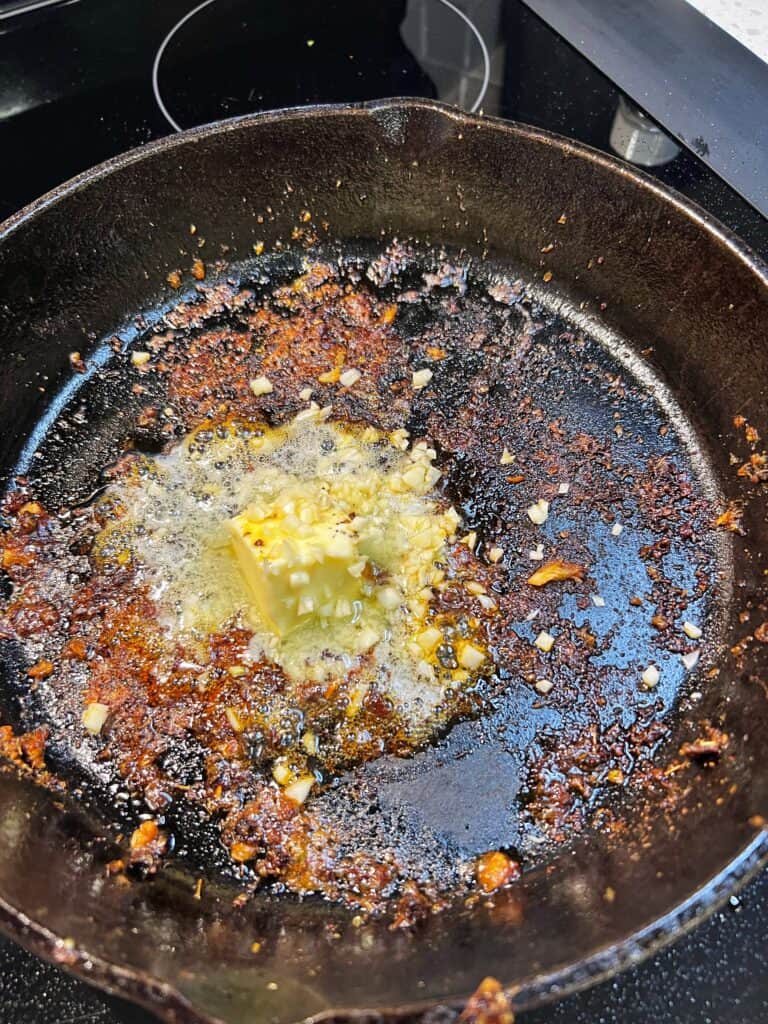 Butter and minced garlic added to a cast iron pan that has browned bits from searing blackened cod.