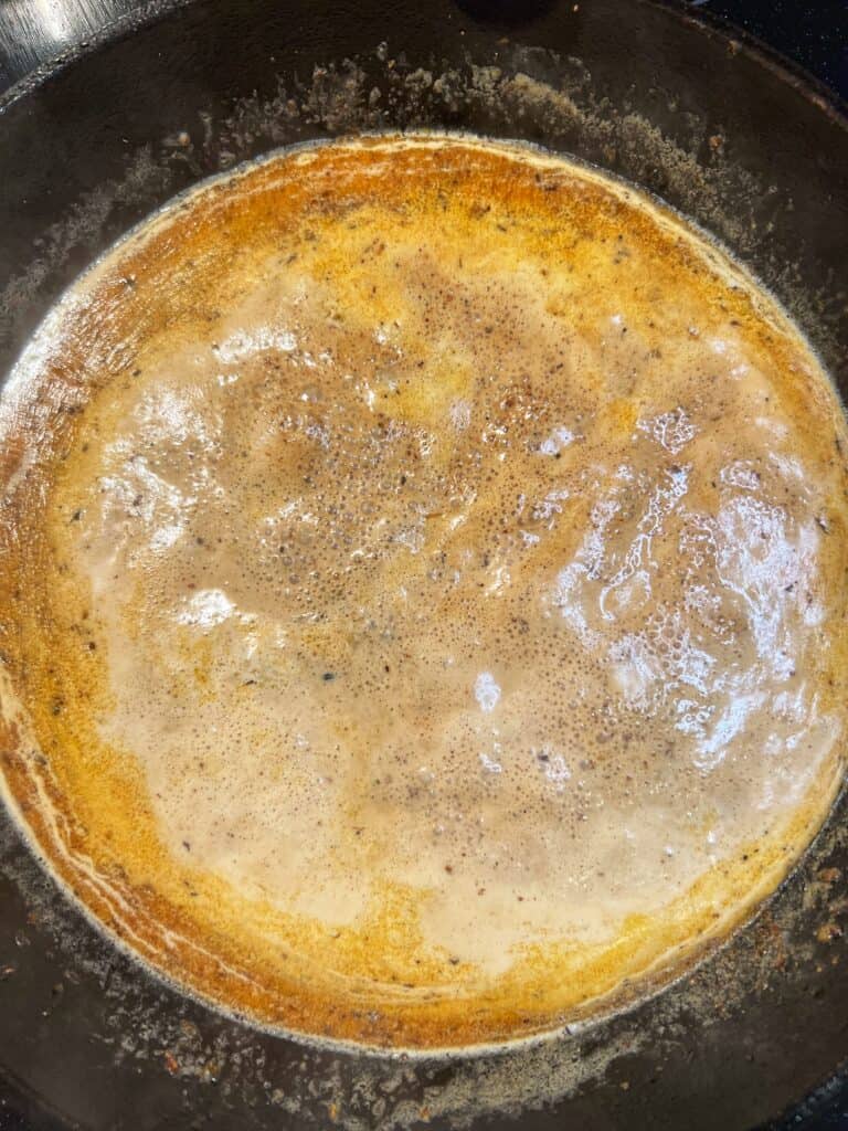 A creamy pan sauce for cod simmering in a cast iron pan.
