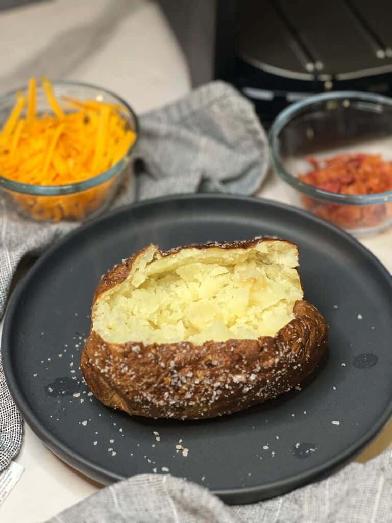 One air fried potato opened up  in the top middle sitting on a charcoal-colored plate.
