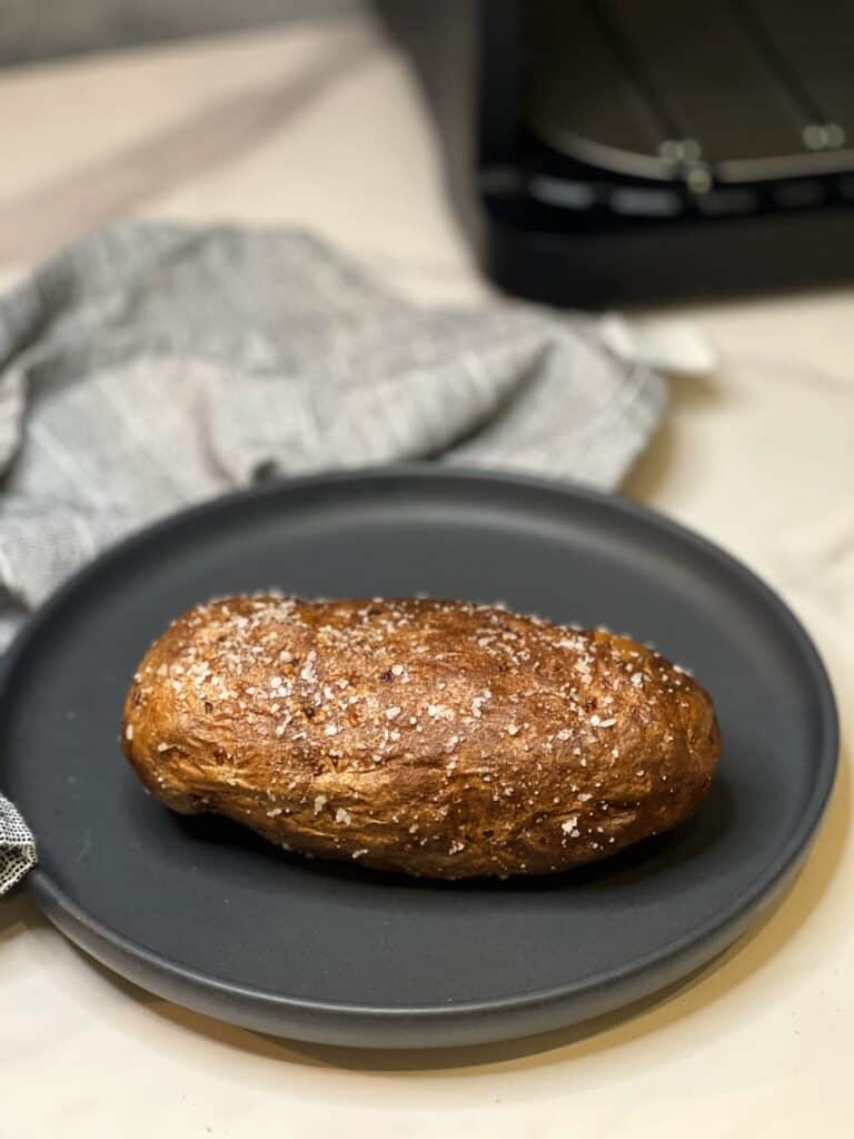 One air fried russet potato sitting on a charcoal-colored plate.