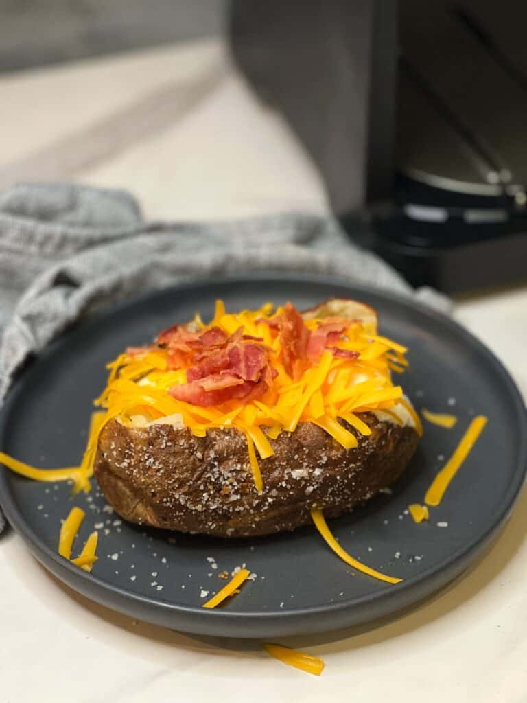 An air fried potato sitting on a charcoal-colored plate loaded with cheese and bacon.