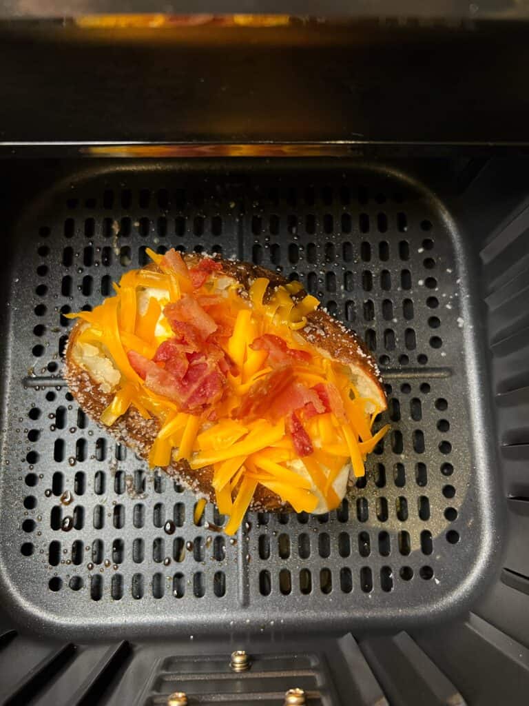 A loaded potato sitting in an air fryer basket.