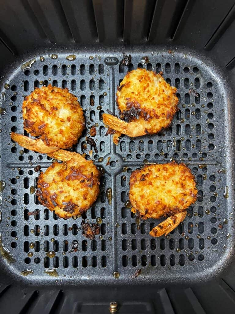Four coconut shrimp sitting in an air fryer basket that have been air fried.