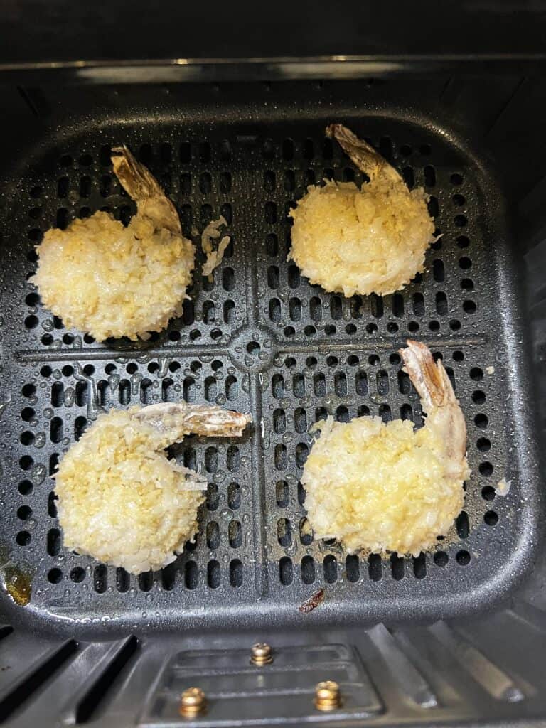 Four coated coconut shrimp sitting in an air fryer basket.