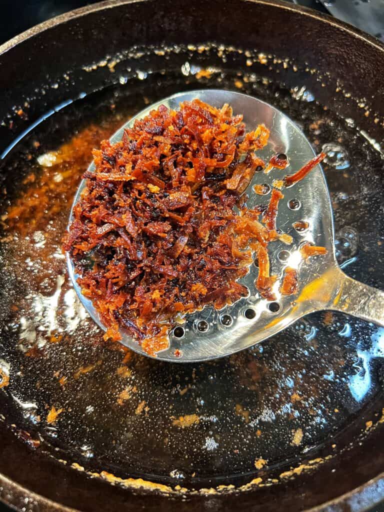A metal slotted spoon holding crispy fried coconut pieces. 