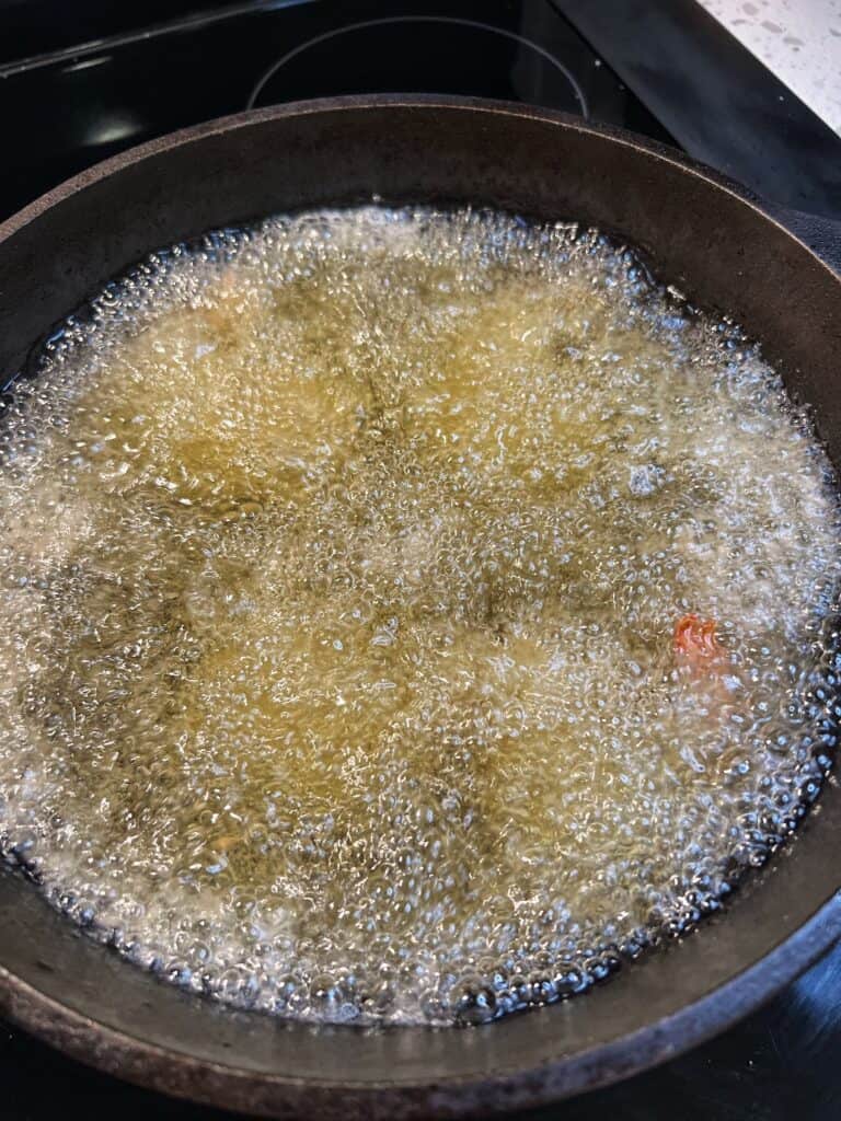 Coconut shrimp frying in cast iron pot full of hot oil.