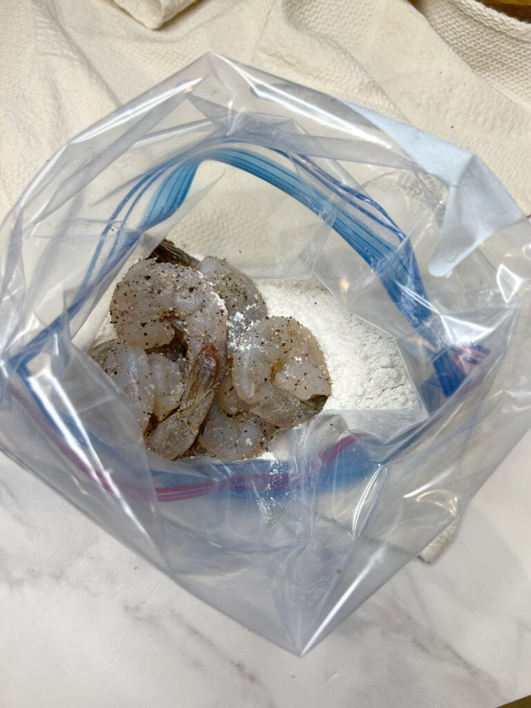 Flour in a freezer bag with seasoned, raw shrimp.