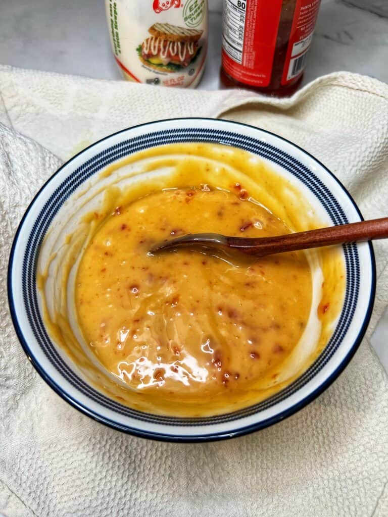 A blue-trimmed white bowl holding a creamy sweet chili sauce with a wooden spoon in the bowl.