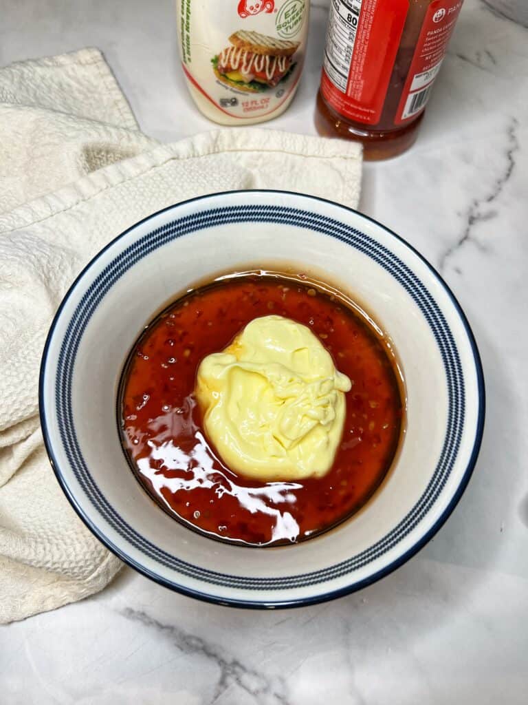 A blue-trimmed white bowl holding sweet chili sauce and kewpie mayo.
