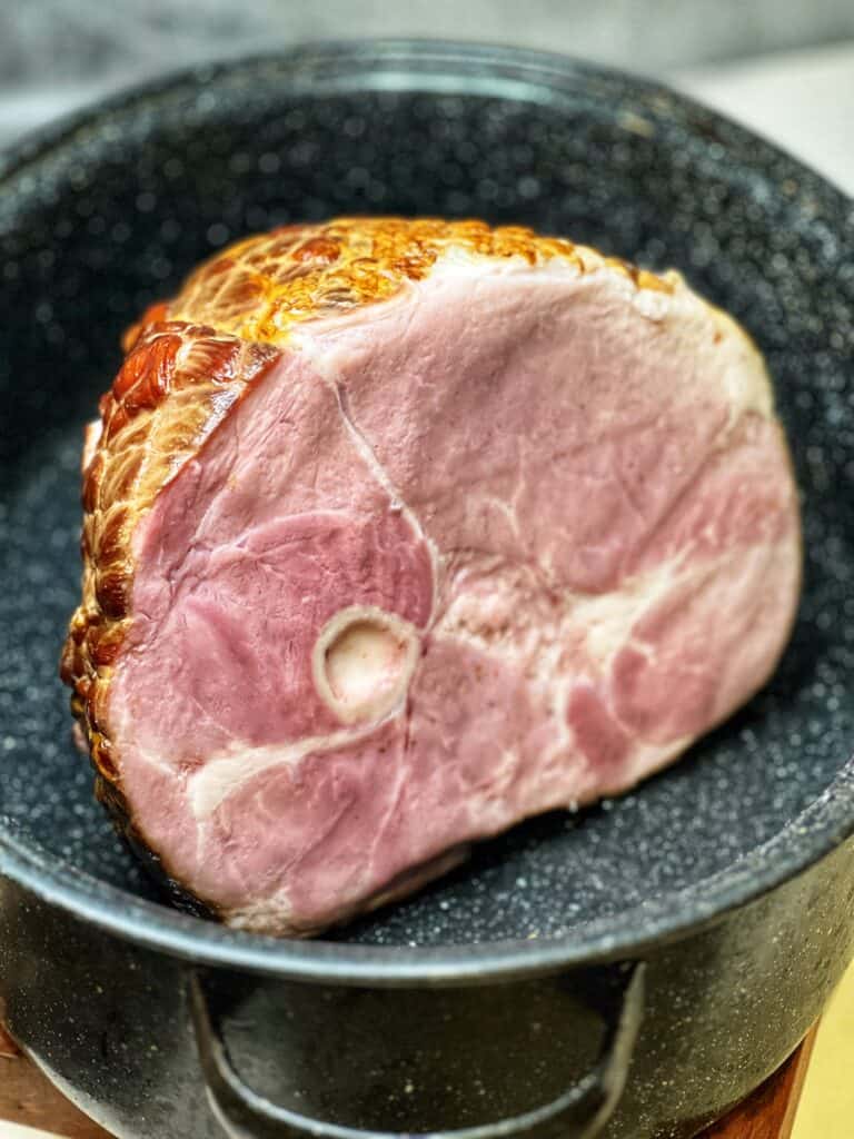 A semi-boneless ham sitting inside of a black speckled roasting pan.