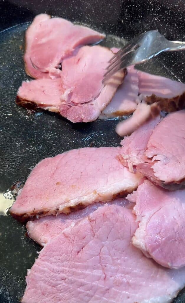 Sliced ham added back to the juices in a roasting pan.