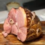 An oven baked semi-boneless ham sitting on a wooden cutting board.