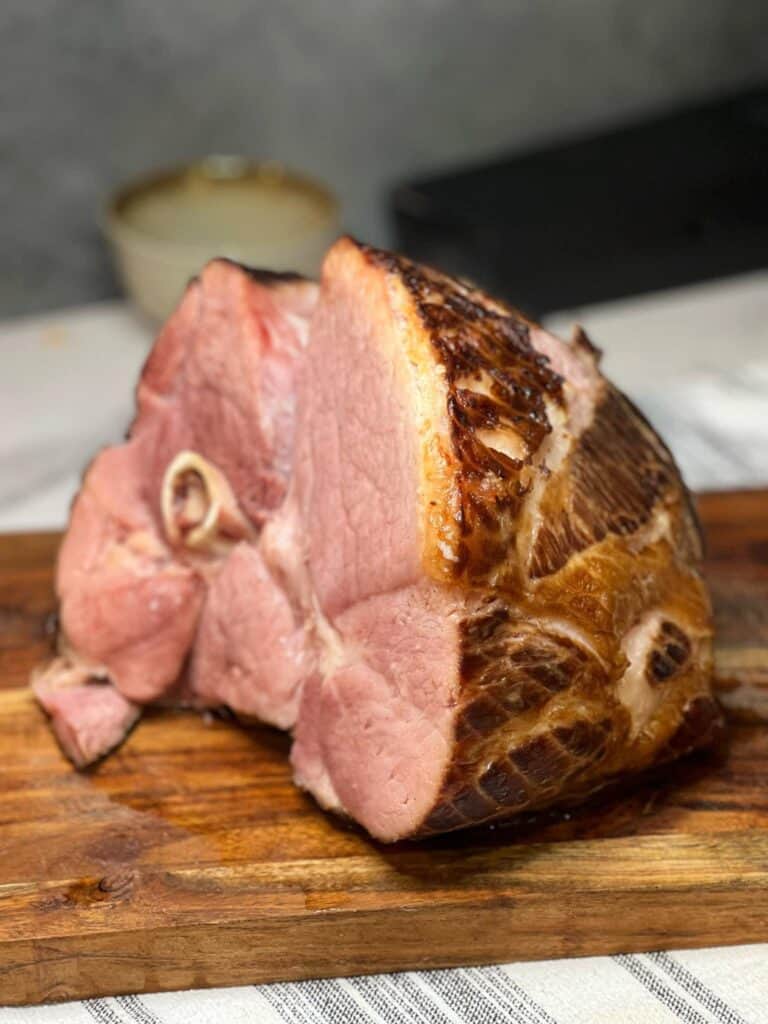 An oven baked semi-boneless ham sitting on a wooden cutting board.