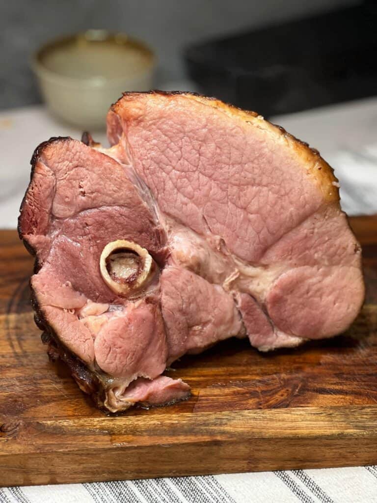 A view of the cut half of an oven baked semi-boneless ham sitting on a wooden cutting board.
