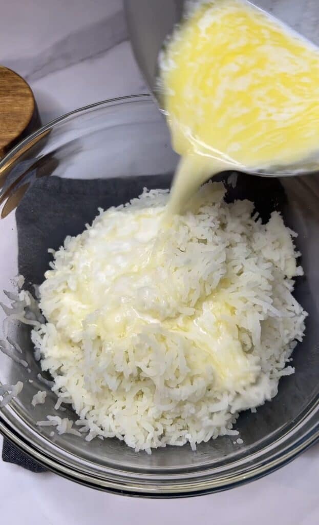 Heated heavy cream and butter being poured into a glass bowl with riced potatoes for creamy mashed potatoes for Easy Bangers and Mash.