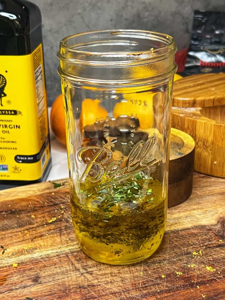 A ball jar filled with ingredients to make a dressing for a salad that will be used to top Haddock Milanese.