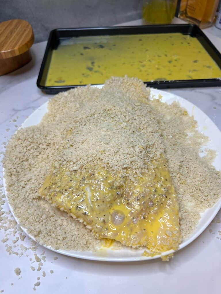 A haddock filet partially coated with beaten egg and panko breadcrumbs.