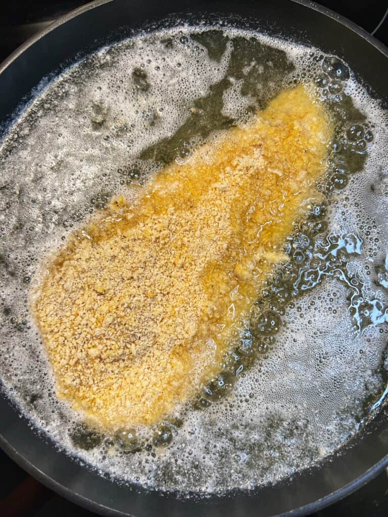 A panko coated haddock filet frying in oil in a non-stick pan.