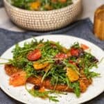 A crispy fried haddock filet topped with an arugula citrus salad sitting on a round, white plate.