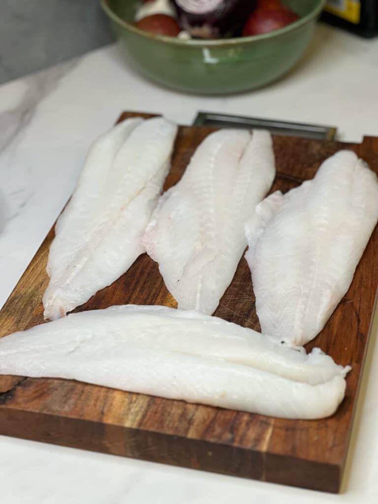 Four large orange roughy filets sitting on a wooden cutting board.
