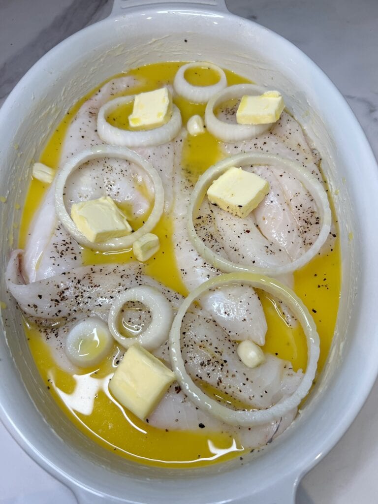 Orange juice poured into a casserole dish that was filled with seasoned orange roughy filets, sliced white onions, garlic and a few pats of butter. 