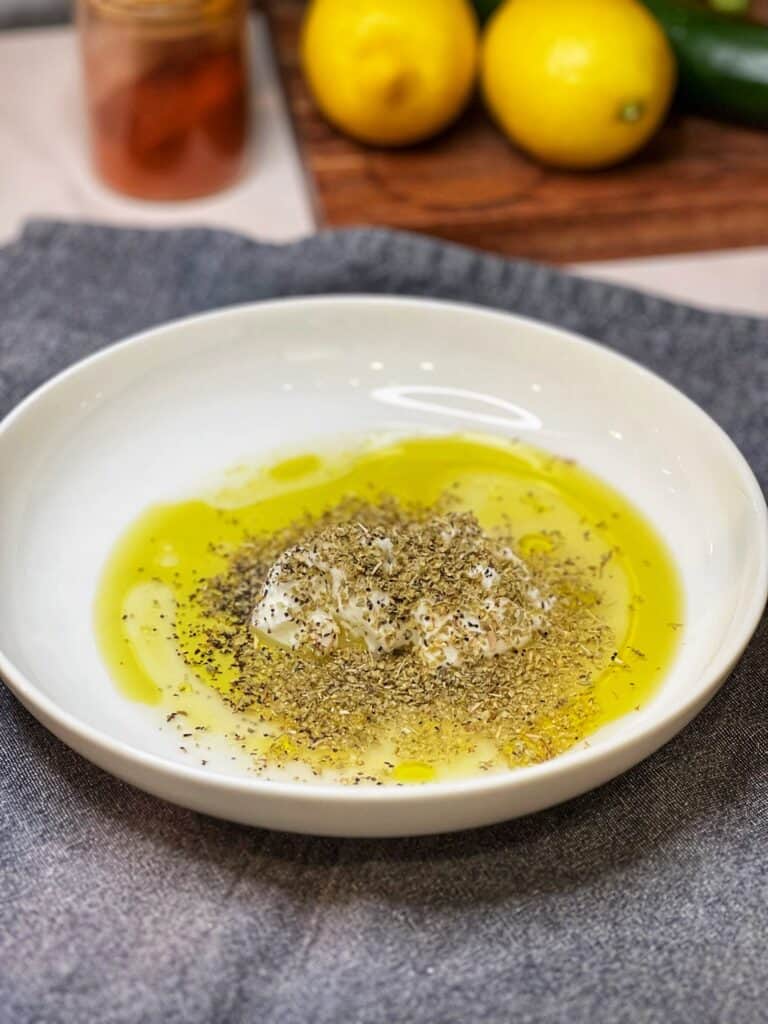 A white bowl of yogurt, olive oil, salt, pepper and dried oregano for a Greek chicken marinade.