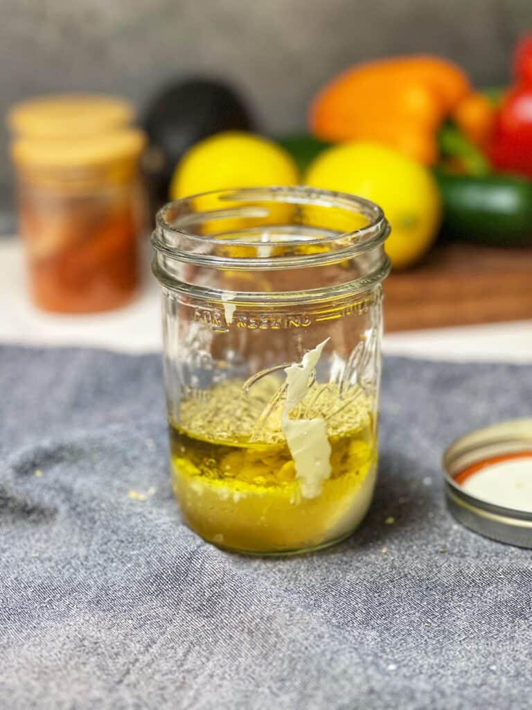 Ingredients for a Greek-style dressing (olive oil, yogurt, herbs, mustard) in a Mason jar ready to be shaken.