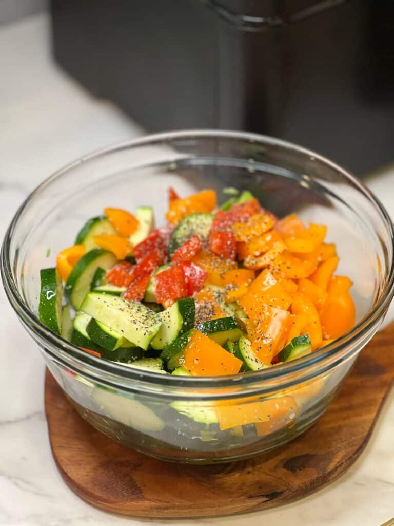 A clear glass bowl filled with chunked zucchini and red and orange bell peppers.