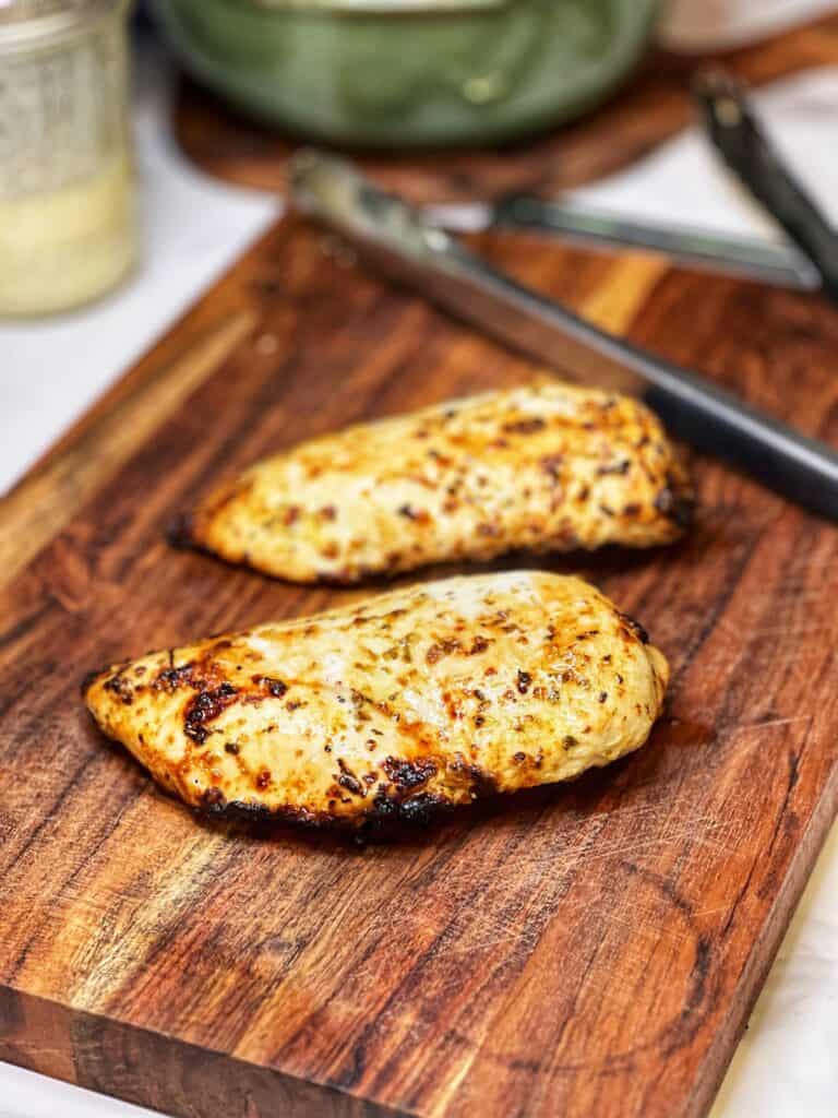 Two air fryer chicken breasts resting on a wooden board before slicing.