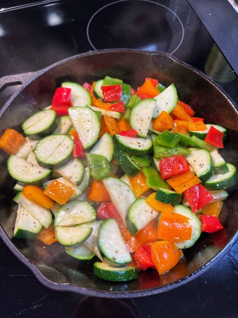 Sautéing zucchini and orange and red bell peppers in a cast iron pan.