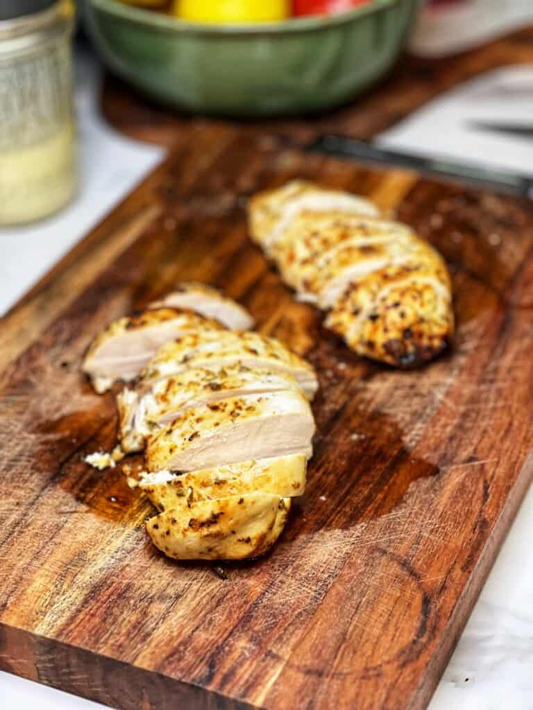 Two sliced Greek-style chicken breasts sitting on a wooden board.