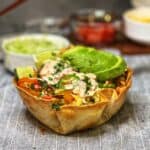 A homemade taco shell bowl filled with ground chicken, bell peppers, jalapeños, sliced avocado and drizzled with taco dressing.