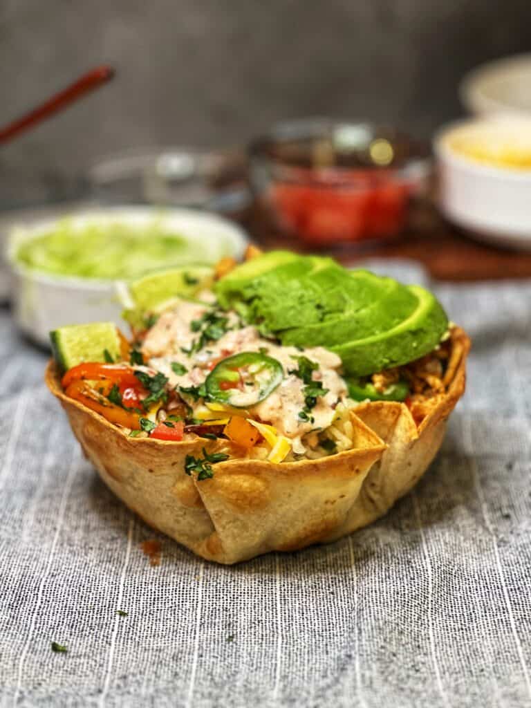 A homemade taco shell bowl filled with ground chicken, bell peppers, jalapeños, sliced avocado and drizzled with taco dressing.