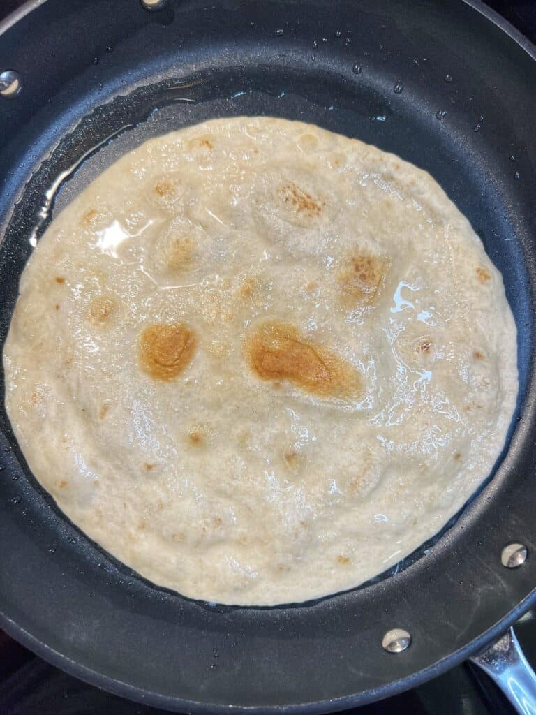 A fried, burrito-sized flour tortilla sitting in a non-stick pan.