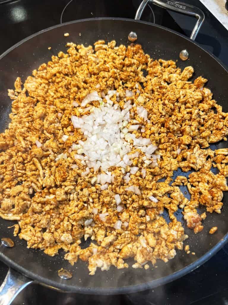 Cooked ground chicken in a non-stick pan with minced garlic and onions added.