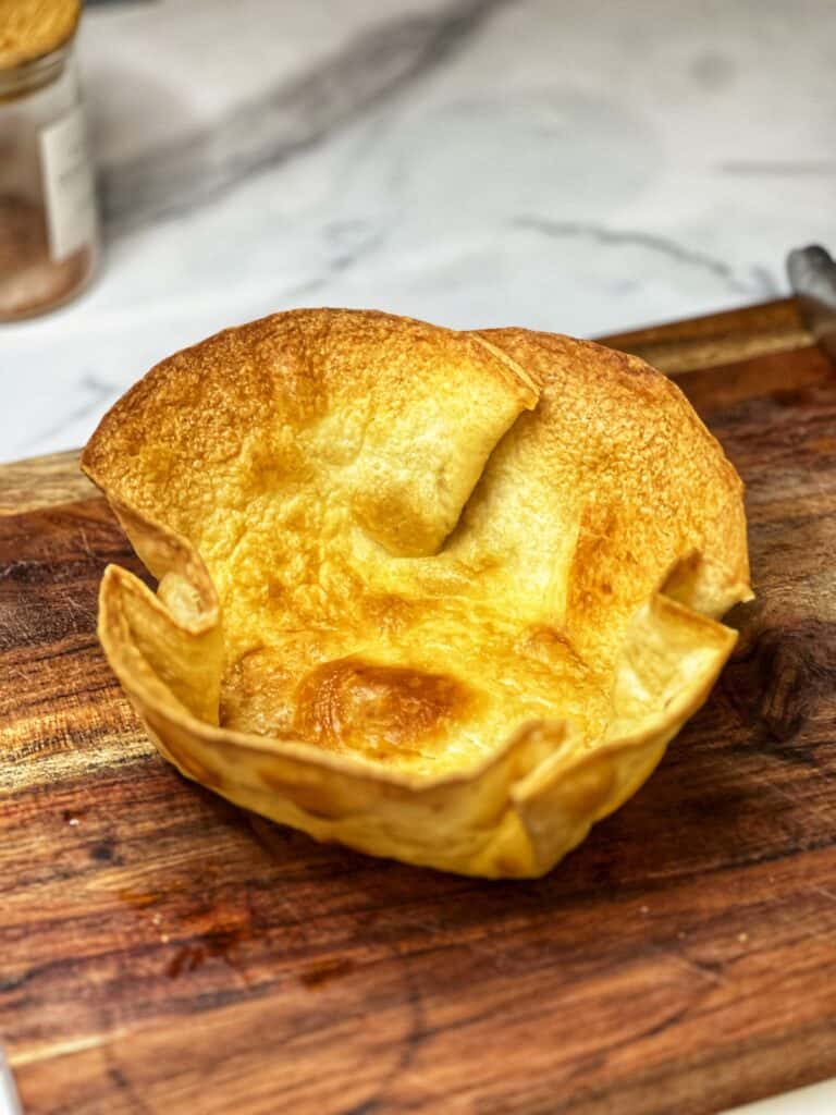 A baked tortilla formed to look like a taco bowl sitting on a wooden board.
